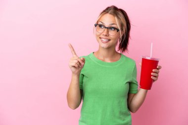Pembe arka planda izole edilmiş bir şekilde serinletici içeceği elinde tutan genç Rus kadın çözümün farkına varmak için parmağını kaldırıyor.