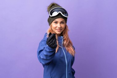 Kar kayağı gözlüklü genç kız izole edilmiş mor arka planda para hareketi yapıyor.