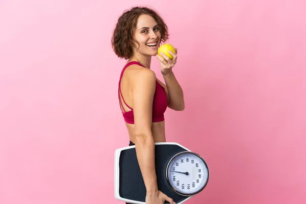 Stock image Young English woman isolated on pink background with weighing machine and with an apple