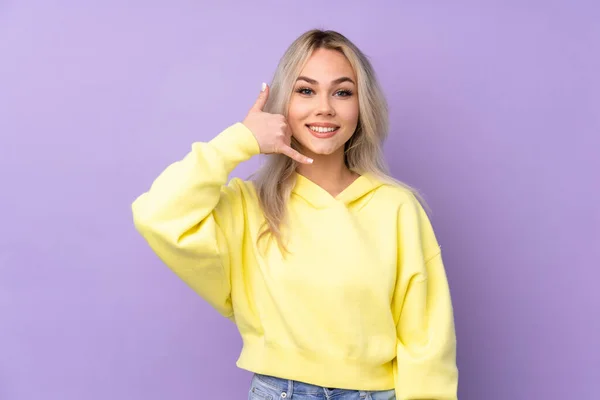 Teenager girl wearing a yellow sweatshirt over isolated purple background making phone gesture. Call me back sign