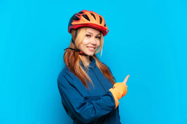 Молодая Девушка Велосипедистка Изолирована Синем Фоне Указывая Назад — стоковое фото