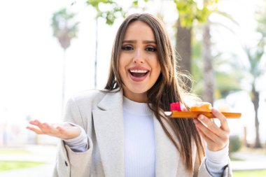 Genç ve güzel bir kadın açık havada sashimi tutuyor ve şok olmuş yüz ifadesi var.