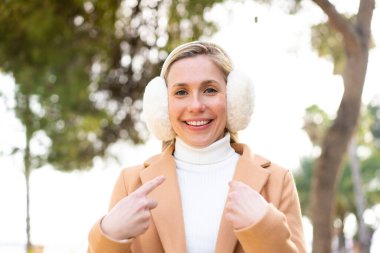 Açık havada, yüzünde sürpriz bir ifade olan, kış maskesi takan genç sarışın kadın.