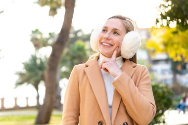 Sarışın genç bir kadın, açık havada kışlık kuklalar takıp yukarı bakarken bir fikir üretiyor.