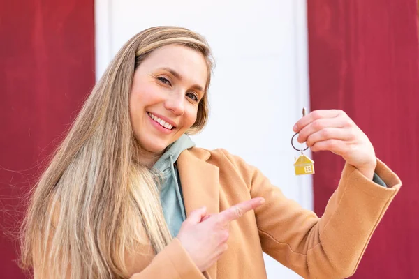 年轻的金发女人在户外拿着家里的钥匙指着它 — 图库照片