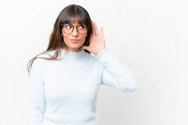 İzole edilmiş beyaz arka planda genç beyaz kadın elini kulağına koyarak bir şeyler dinliyor.