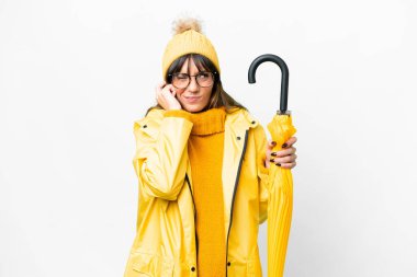 Young caucasian woman with rainproof coat and umbrella over isolated white background frustrated and covering ears