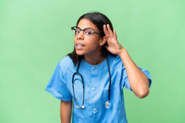 Genç Afrikalı Amerikalı hemşire, izole edilmiş arka planda bir şey dinlerken elini kulağına koydu.