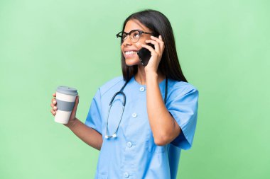 Genç Afrikalı Amerikalı hemşire, izole edilmiş arka planda kahve ve cep telefonu tutuyor.