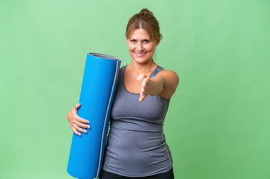 Orta yaşlı sporcu kadın yoga derslerine gidiyor. Elinde paspas, izole bir arka planda. İyi bir anlaşma için el sıkışıyor.