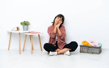 Genç melez kadın, beyaz arka planda izole bir şekilde yerde oturan kıyafetleri katlıyor ve hareketli bir uyku hareketi yapıyor.