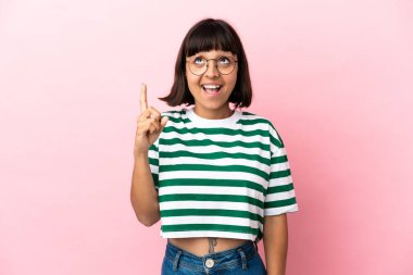 Pembe arka planda izole edilmiş genç melez kadın yukarı bakıyor ve şaşırıyor.