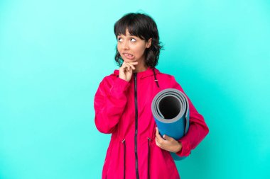 Mavi arka planda bir minder tutarken yoga derslerine giden genç kız kuşkuları ve düşünceleri var.