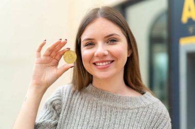 Genç, güzel sarışın kadın elinde mutlu bir ifadeyle Bitcoin tutuyor.