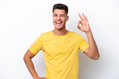 Beyaz arka planda izole edilmiş genç beyaz adam parmaklarıyla tamam işareti gösteriyor.