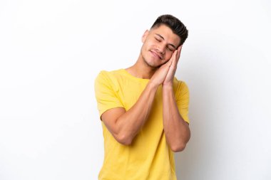 Beyaz arka planda izole edilmiş genç beyaz bir adam uyku jesti yapıyor.