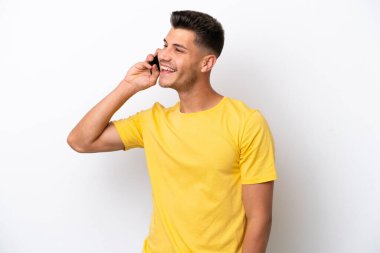 Beyaz arka planda izole edilmiş genç beyaz bir adam cep telefonuyla sohbet ediyor.