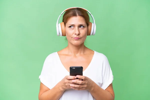 Middle Aged Caucasian Woman Isolated Background Listening Music Mobile Thinking — Stock Photo, Image