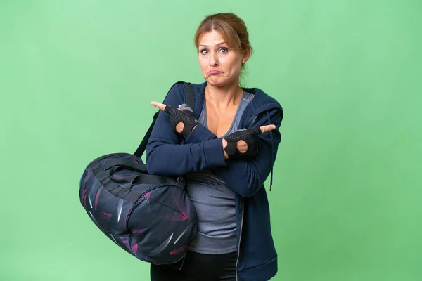 スポーツバッグを持つ中年のスポーツ女性は 疑いを持っているラテラルを指して隔離された背景に — ストック写真