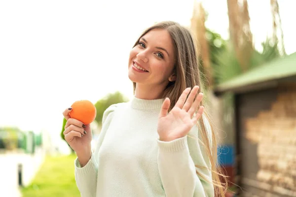 Ung Söt Blond Kvinna Håller Apelsin Utomhus Saluterar Med Handen — Stockfoto
