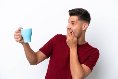 Beyaz arka planda, şaşırmış ve şok olmuş bir yüz ifadesiyle bir fincan kahve tutan beyaz bir adam.