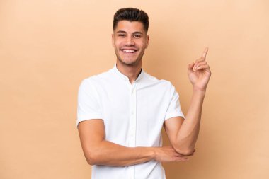Beyazlı genç adam bej arka planda izole edilmiş, mutlu ve dik duruyor.