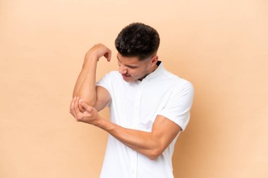 Young caucasian man isolated on beige background with pain in elbow