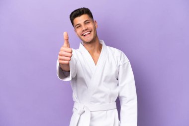 Young caucasian man doing karate isolated on purple background with thumbs up because something good has happened