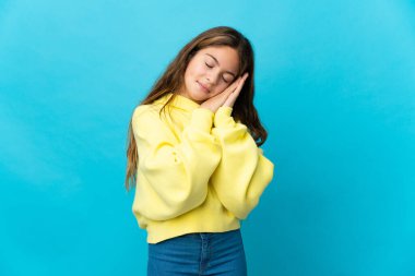 Küçük kız mavi arka plan üzerinde uyku jesti yapıyor.