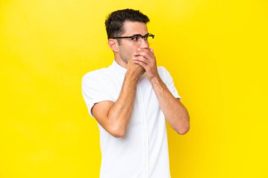 Genç yakışıklı adam, izole edilmiş sarı arka planda ağzını kapatıyor ve yan tarafa bakıyor.