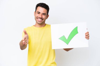 İzole edilmiş beyaz bir geçmişi olan genç yakışıklı bir adam üzerinde yeşil işaret simgesi olan bir pankart tutuyor ve anlaşma yapıyor.