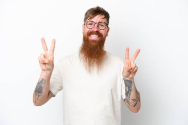 Kızıl saçlı uzun sakallı adam beyaz arka planda iki eliyle zafer işareti gösteriyor.