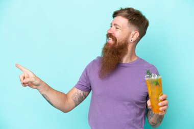 Uzun sakallı kızıl saçlı bir adam mavi arka planda izole edilmiş bir kokteyl tutuyor.