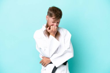 Redhead man with long beard doing karate isolated on blue background having doubts
