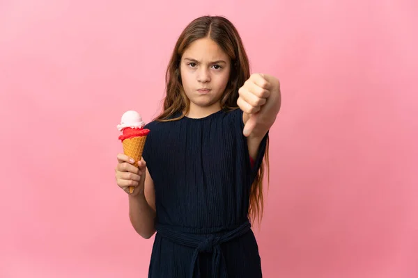孤立したピンクの背景の上にコーンアイスクリームを持つ子供は 負の式で親指を示しています — ストック写真