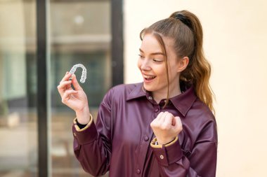 Genç ve güzel bir kız, dışarıda görünmez diş telleriyle zaferi kutluyor.