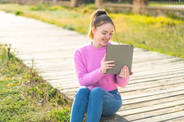 Genç ve güzel bir kız elinde tabletle dışarıda mutlu bir ifadeyle bekliyor.