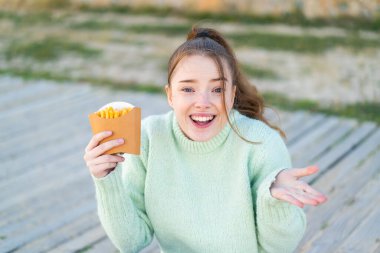 Genç ve güzel bir kız, açık havada yüzünde şok ifadesi olan kızarmış cipsler tutuyor.