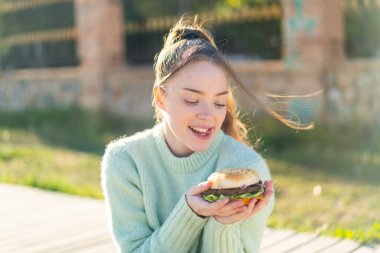 Genç ve güzel bir kız elinde hamburgerle dışarıda