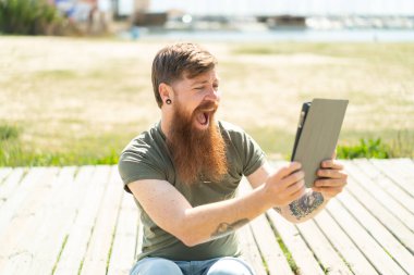 Kızıl saçlı, sakallı, elinde tablet olan, şaşırmış bir adam.