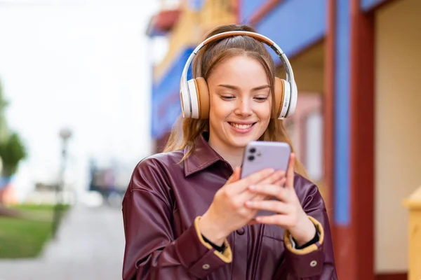 Молодая Симпатичная Девушка Улице Слушает Музыку Смотрит Мобильный Телефон — стоковое фото