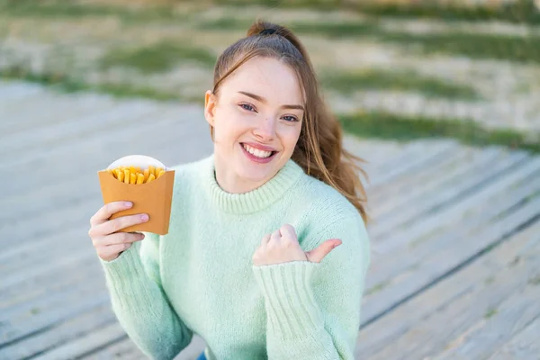 Young Pretty Girl Holding Fried Chips Outdoors Pointing Side Present — Stock Photo, Image