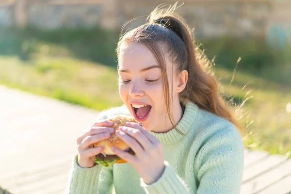 Młoda Ładna Dziewczyna Trzyma Hamburgera Świeżym Powietrzu — Zdjęcie stockowe