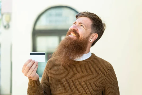 Zrzavý Muž Plnovousem Drží Kreditní Kartu Venku Dívá Nahoru Usmívá — Stock fotografie