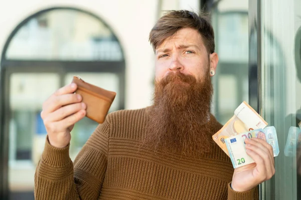 Рыжий Бородой Держит Бумажник Деньгами Сомневается — стоковое фото