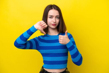 Sarı arka planda izole edilmiş genç Ukraynalı kadın iyiye-kötüye işaret veriyor. Evet ya da hayır arasında kararsız