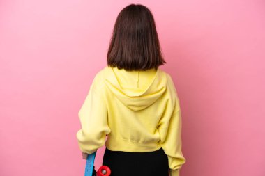 Young Ukrainian woman isolated on pink background with a skate in back position