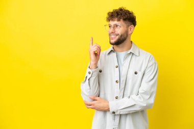 Sarı arka planda izole edilmiş yakışıklı beyaz adam harika bir fikre işaret ediyor.