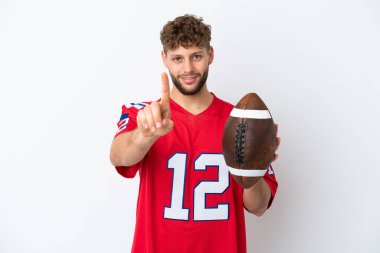 Beyaz arka planda ragbi oynayan beyaz bir adam parmak kaldırıyor.