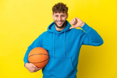 Sarı arka planda izole edilmiş yakışıklı beyaz adam basketbol oynuyor ve kendisiyle gurur duyuyor.